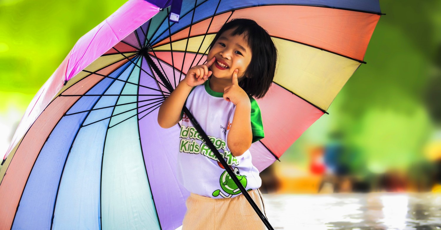Ein kleines Mädchen hält einen riesigen bunt gestreiften Regenschirm und lacht