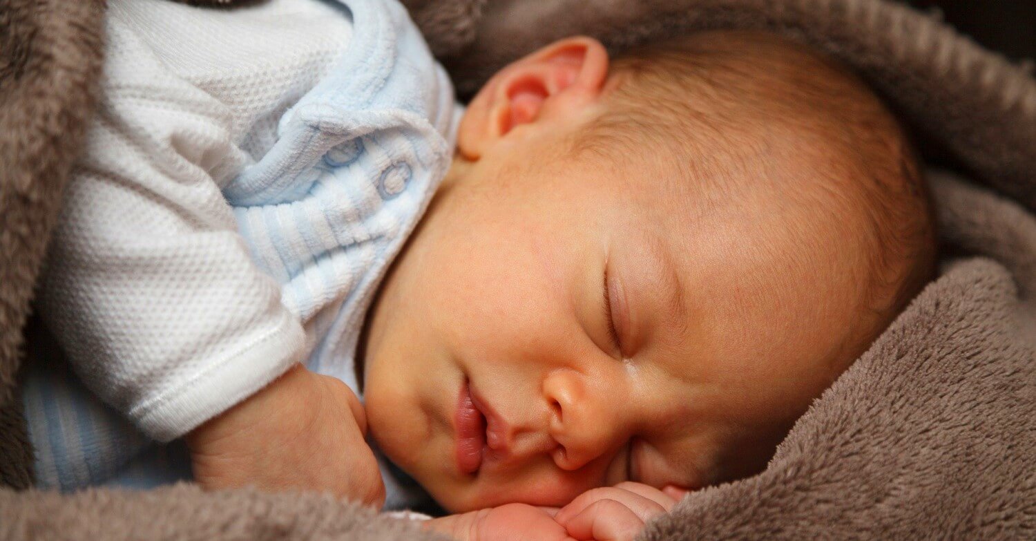 Baby in weißem Strampelanzug schläft in Kuscheldecke gewickelt