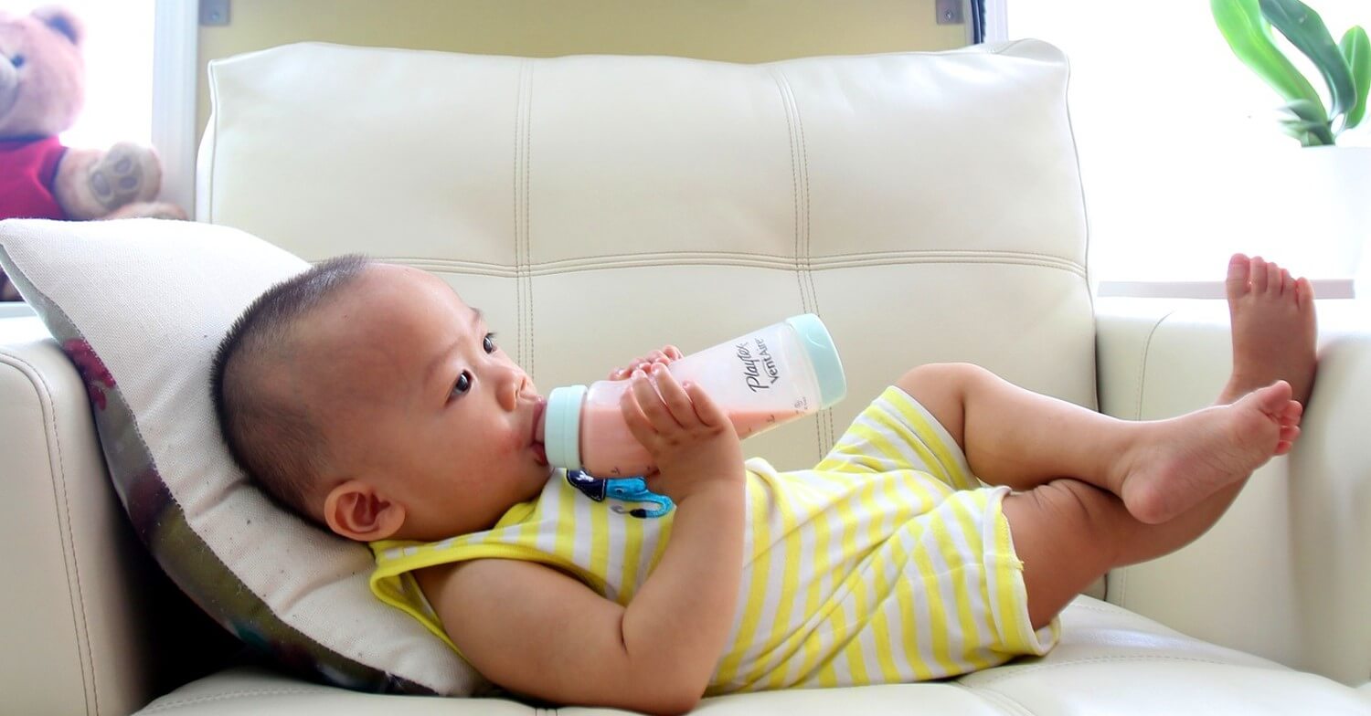 Ein Baby liegt in einem Sessel und trinkt Milch aus seinem Fläschchen