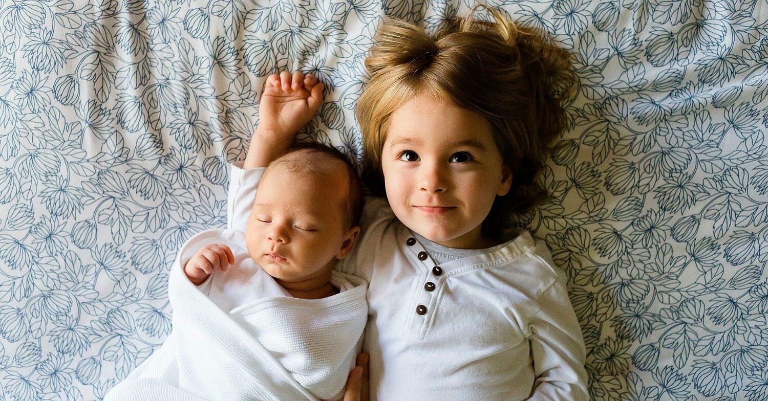 Geschiwster: ein kleiner Junge hält seine neugeborene Schwester im Arm