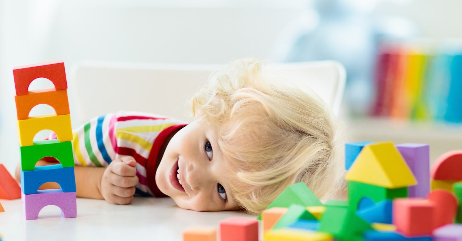 Ein blondes kleines Kind spielt mit bunten Bauklötzen