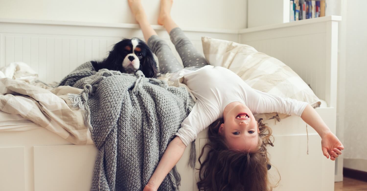 Ein junges Mädchen turnt auf ihrem Bett herum, neben ihr liegt ein kleiner Hund