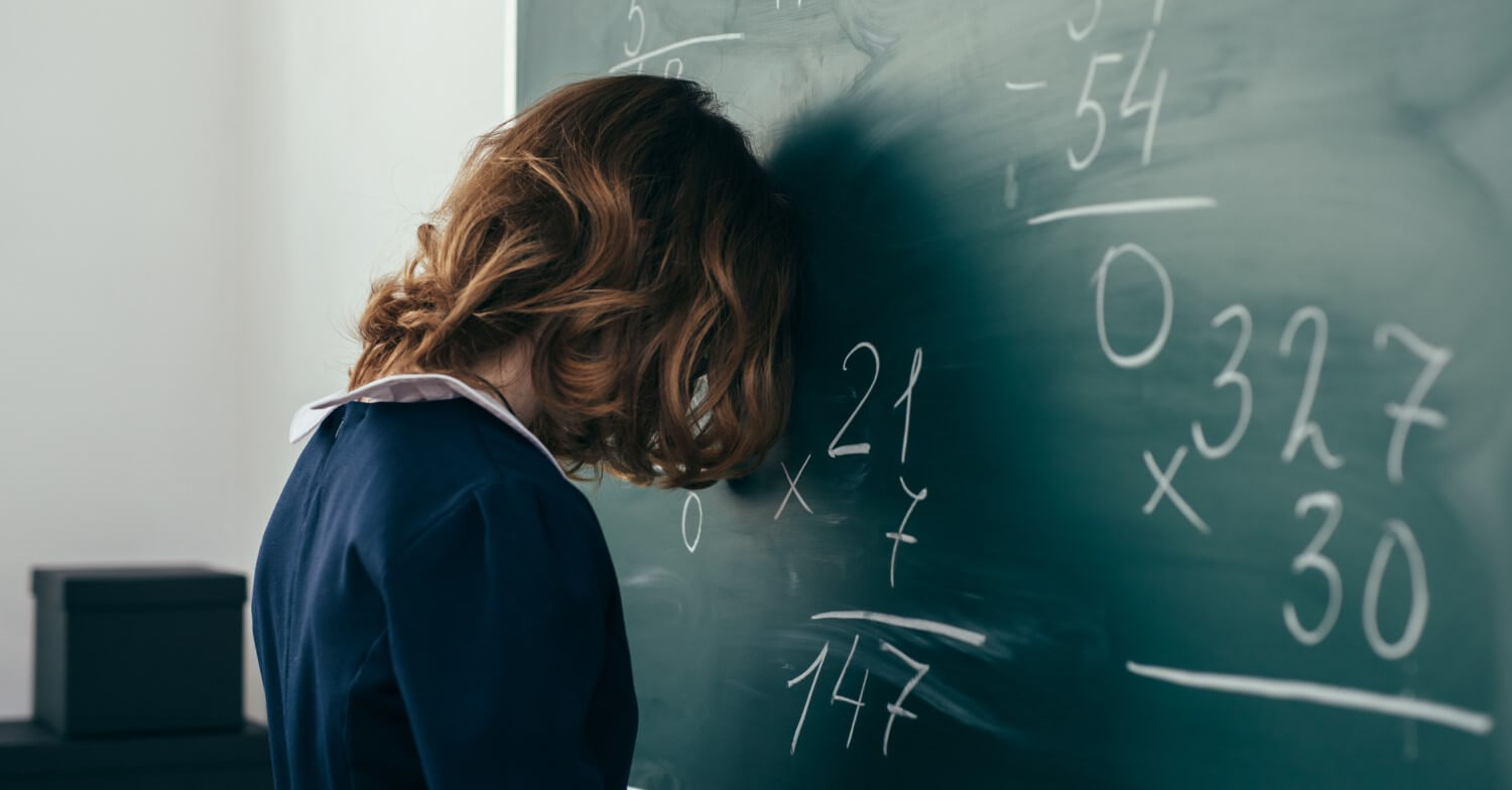 Eine Schülerin weiß im Matheunterricht nicht weiter und lehnt den Kopf gegen die Tafel