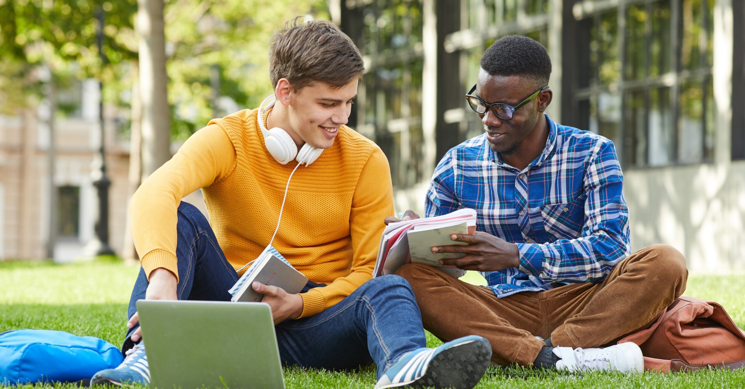 Zwei Schüler im Teenageralter sitzen auf dem Rasen und lernen