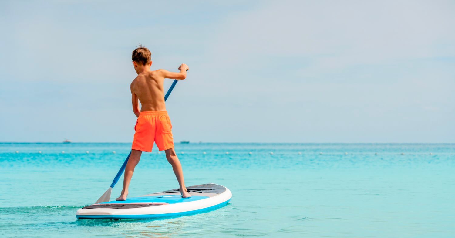 Ein Junge steht mit einem Paddel auf einem Surfbrett und paddelt über einen See