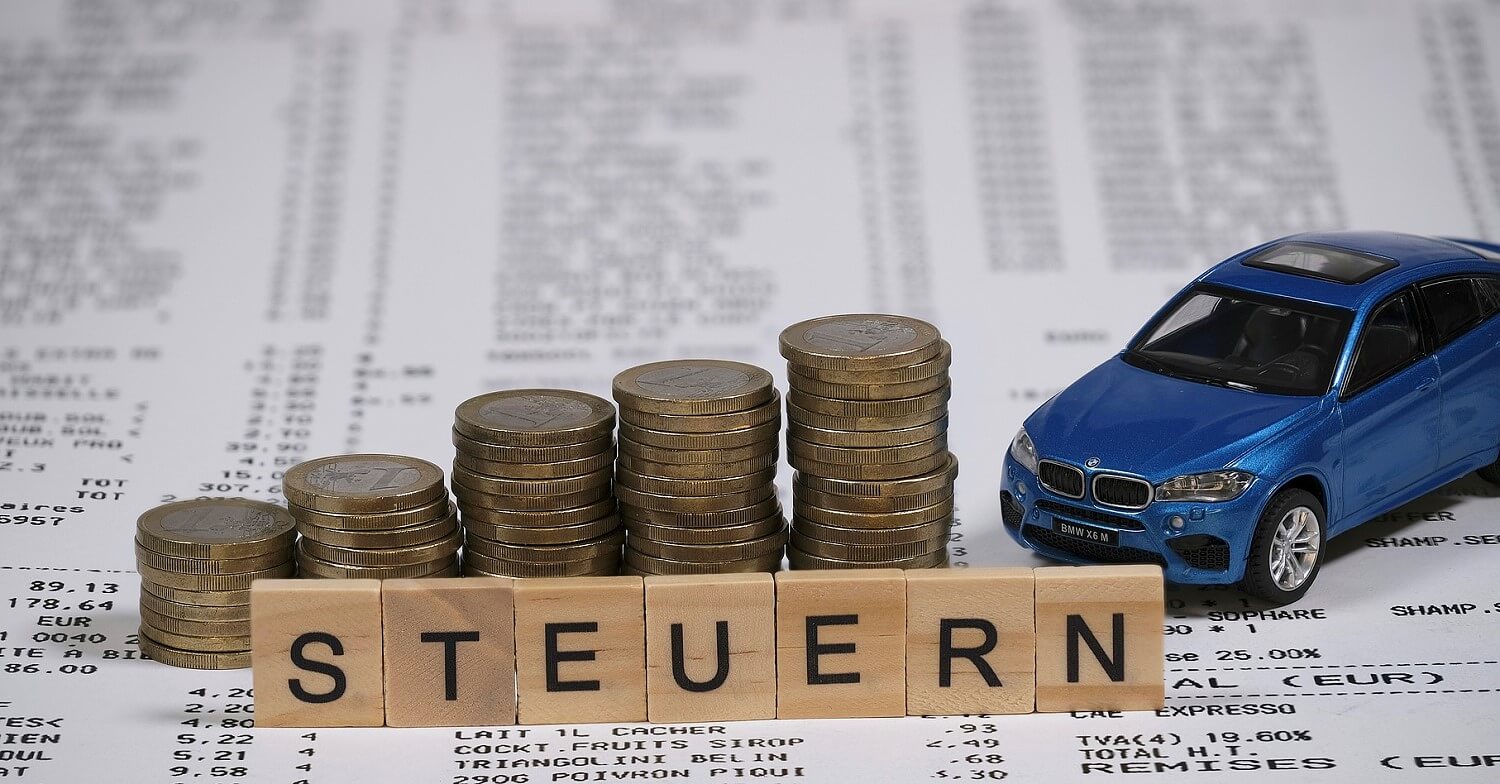 Steuern: mehrere Stapel Münzen und ein Spielzeugauto auf den Steuerunterlagen