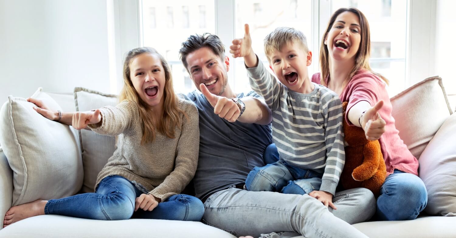 Eine lachende Familie mit zwei Kindern sitzt auf dem Sofa